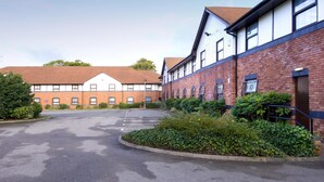 A building with a parking lot, a mix of brick and white walls, and some greenery. - Premier Inn Liverpool - West Derby (Liverpool)