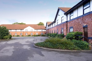 A building with a parking lot, a mix of brick and white walls, and some greenery. - Premier Inn Liverpool - West Derby (Liverpool)