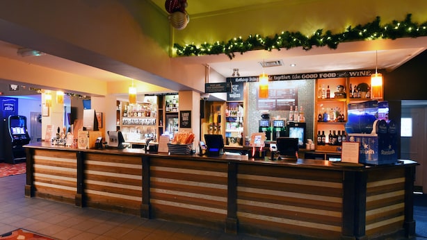 Un espace bar avec un comptoir, des étagères remplies de bouteilles et un panneau sur lequel on peut lire : « Rien ne rapproche autant que la bonne nourriture et le bon vin. »