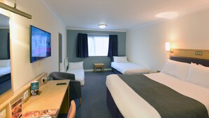 Une chambre d’hôtel avec deux lits simples, un bureau avec une chaise, une petite table, un téléviseur et une fenêtre avec des rideaux.