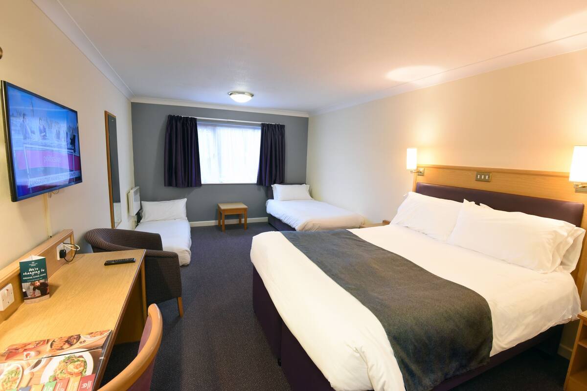 A hotel room with two beds, a desk, a chair, a television, and a window with curtains.
