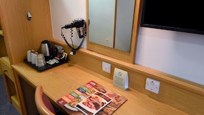 Une chambre d’hôtel avec un bureau en bois, un sèche-cheveux, un plateau avec des articles de toilette, un miroir et un panneau indiquant qu’il est interdit de fumer.