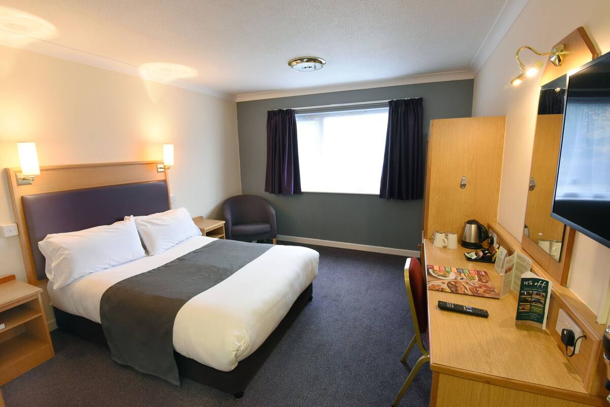 A hotel room with a bed, desk, chair, and a window with curtains.