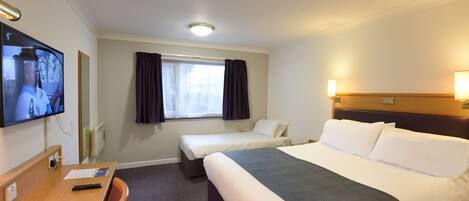 A hotel room with a large bed, a smaller bed, a desk with a TV, and a window with curtains.