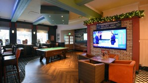 Une salle de billard équipée d’une table de billard, de sièges confortables et d’un téléviseur diffusant un événement sportif.