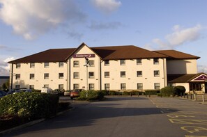 Ein Hotel mit einem Schild 'Premier Inn' an der Fassade, einem Parkplatz und blauem Himmel.