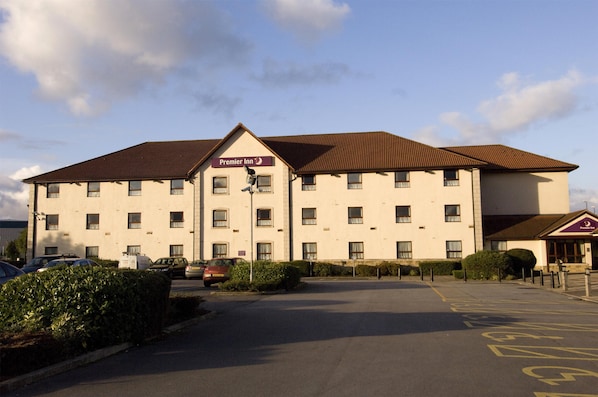 Un hĂŽtel dont la façade porte lâenseigne « Premier Inn », avec un parking et un ciel dĂ©gagĂ©.