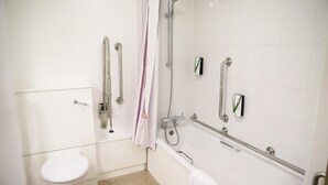 Un baño con inodoro, ducha con barras de apoyo y bañera con cabezal de ducha manual.