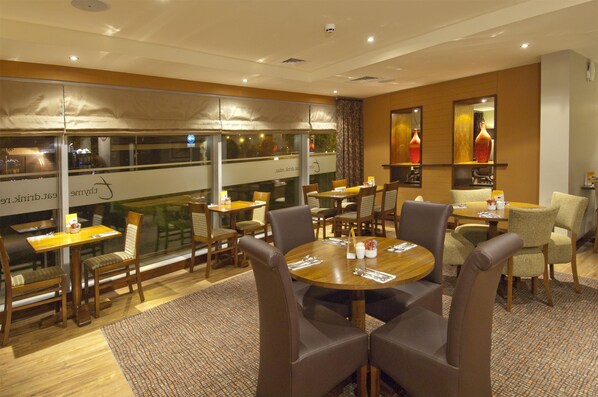 A hotel dining area with multiple tables and chairs, large windows, and a view of the city. - Premier Inn Liverpool John Lennon Airport (Liverpool)