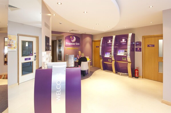 A hotel reception area with a 'WELCOME' sign, a receptionist, and Premier Inn branding. - Premier Inn Liverpool John Lennon Airport (Liverpool)