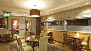 Ein Hotel-Essbereich mit einem großen runden Tisch, mehreren Stühlen, einer Hängeleuchte und einem Fenster mit Vorhängen.