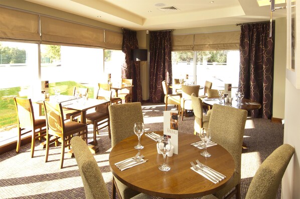 A dining area with round tables, chairs, and a menu stand. - Premier Inn Liverpool John Lennon Airport (Liverpool)
