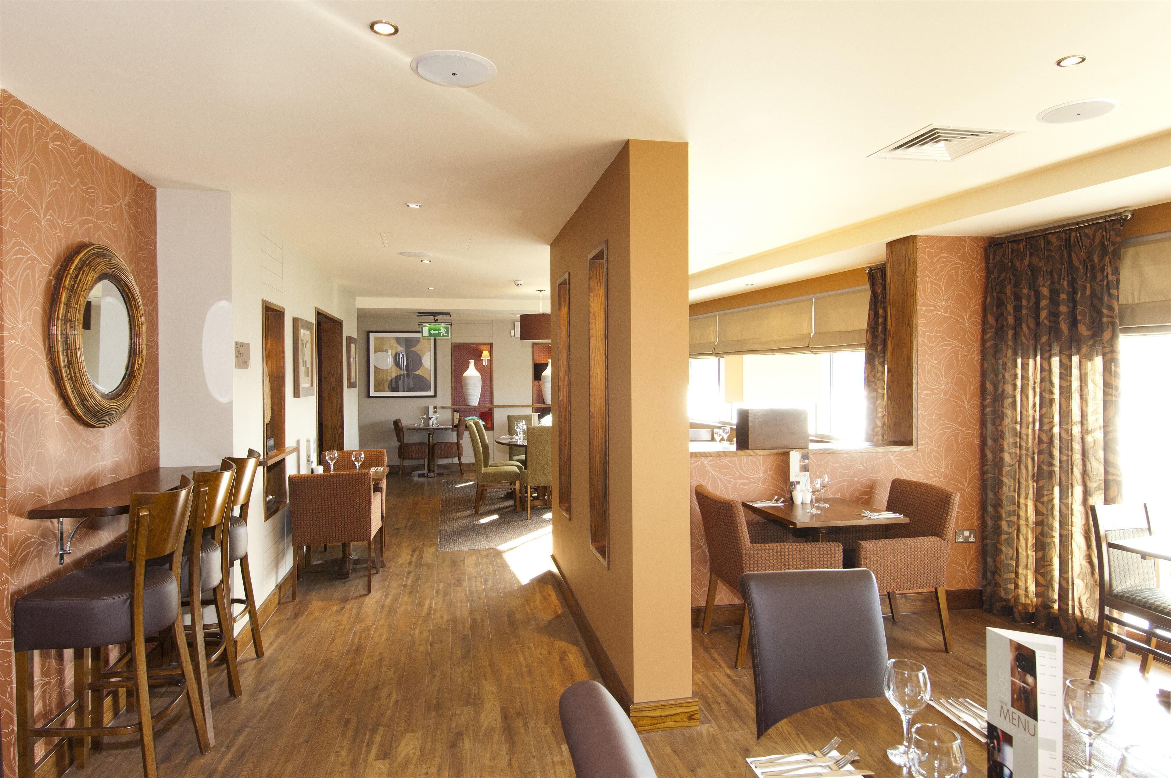 Ein Speisebereich eines Hotels mit Holztischen und -stühlen, eine Bar und eine Rezeption.