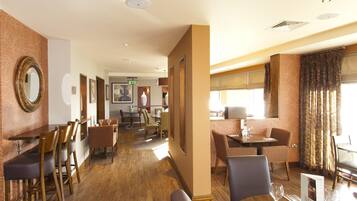 Ein Speisebereich eines Hotels mit Holztischen und -stühlen, eine Bar und eine Rezeption.