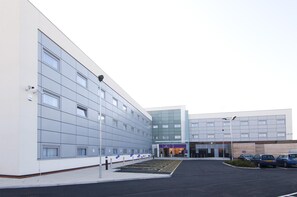 A modern building with a parking lot, a covered entrance, and a few parked cars. - Premier Inn Liverpool John Lennon Airport (Liverpool)