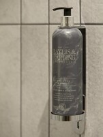 A Baylis & Harding Elements bottle with a pump dispenser, placed on a tiled wall.