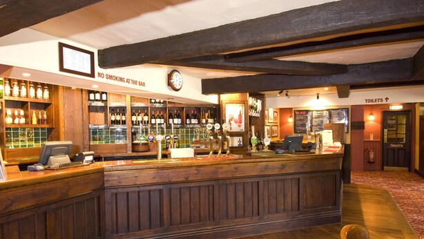 A bar area with wooden furnishings, a clock, and a sign indicating no smoking. - Premier Inn Tring (Tring)