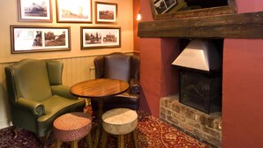 A room with a fireplace, leather armchairs, a round wooden table, and framed photographs on the wall. - Premier Inn Tring (Tring)