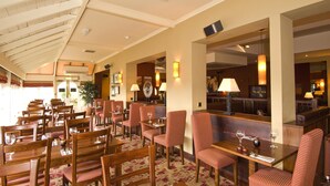 A hotel dining area with wooden tables and chairs, a patterned carpet, and a ceiling with wooden beams. - Premier Inn Tring (Tring)