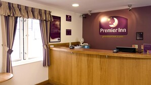 A hotel reception desk with a sign for Premier Inn, a window with curtains, and a wall-mounted fan.