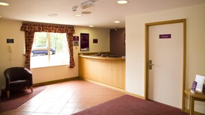 A reception area with a desk, a chair, a private door, and a window with a view of the outside. - Premier Inn Watford North (Watford)