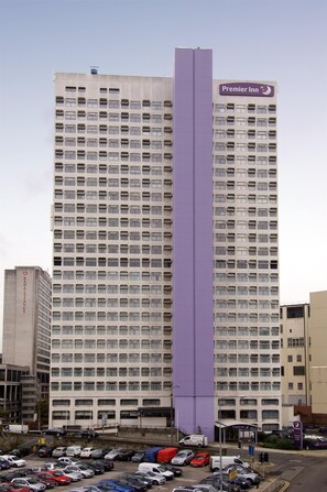 Ein hohes Hotelgebäude mit einem auffälligen, violetten vertikalen Streifen, zahlreichen Stockwerken und einem Parkplatz davor.