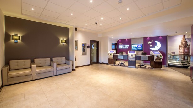 A hotel lobby with a reception desk, self-service kiosks, a chandelier, and a display case. - Premier Inn Manchester - Arena/Printworks (Manchester)