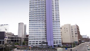 A tall hotel with a prominent purple vertical feature, multiple floors, and a clear sky. - Premier Inn Manchester - Arena/Printworks (Manchester)