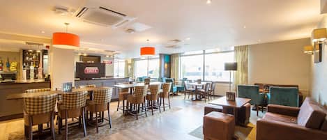 A hotel lobby with a bar, dining area, and seating.