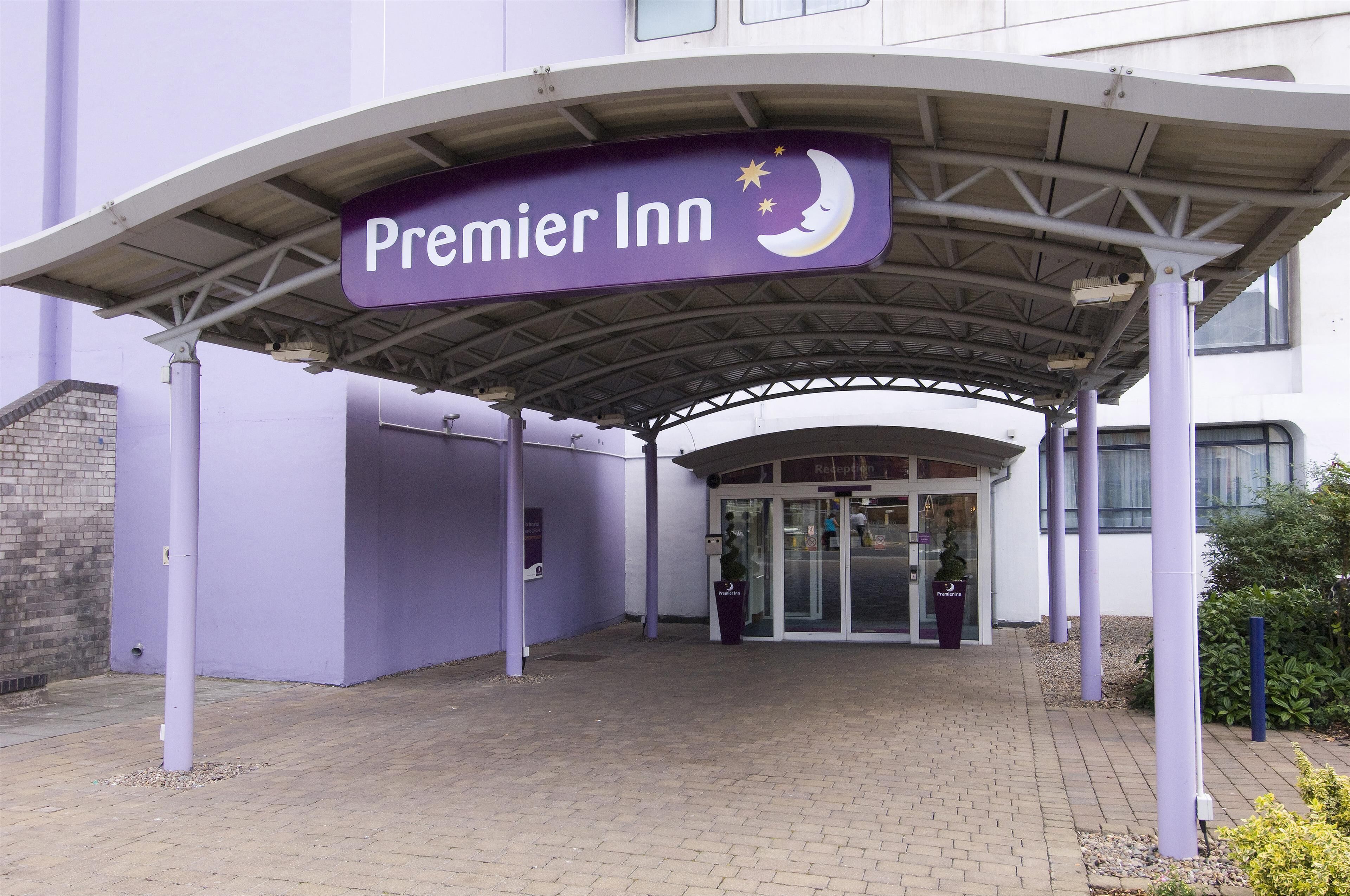 A hotel entrance with a covered walkway, a sign for Premier Inn, and a glass door entrance.