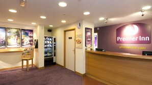 Ein Hotel-Empfangsbereich mit einem Holztresen, einem Verkaufsautomaten und Informationsplakaten an den Wänden.