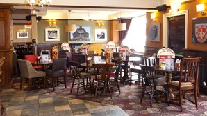 Ein Restaurant mit Holztischen, einem gemusterten Teppich und Wanddekorationen, darunter gerahmte Bilder und ein Wappen.