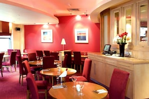 A restaurant with red walls, wooden tables, and red chairs. - Premier Inn Manchester Portland St (Manchester)