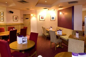 A hotel lobby with round tables, red and beige chairs, a sofa, framed pictures on the walls, and a reception desk. - Premier Inn Manchester Portland St (Manchester)