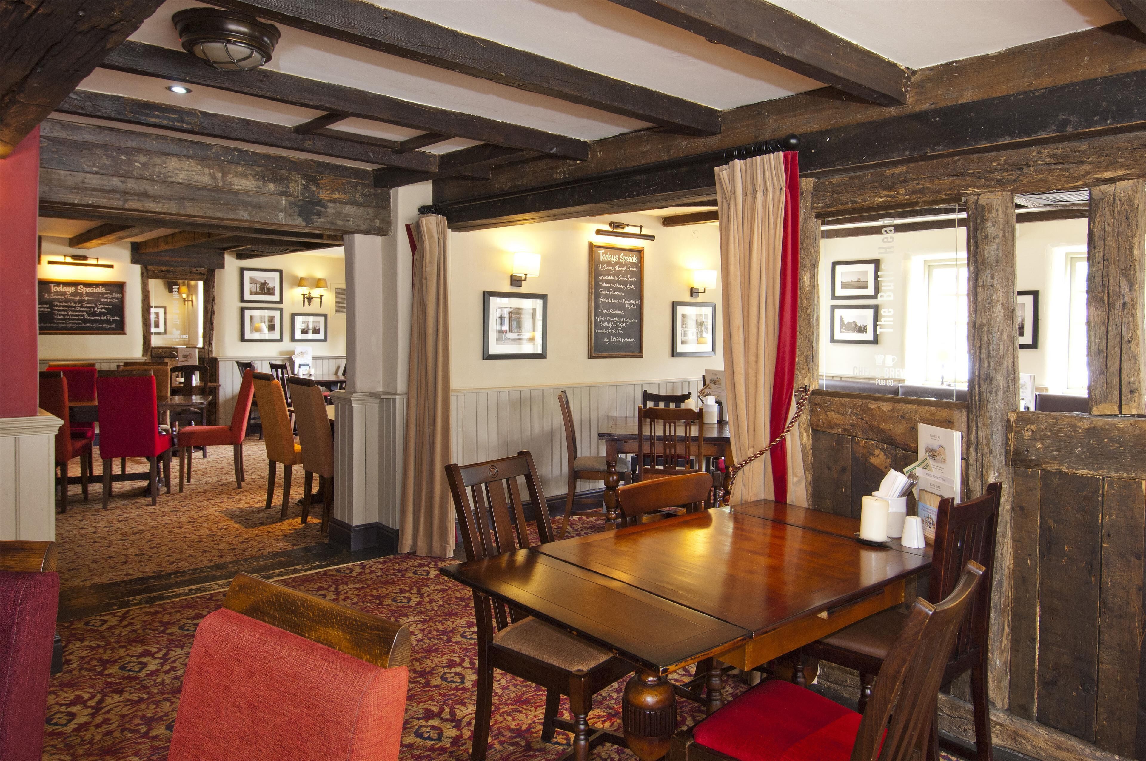 A traditional inn with a wooden dining table, red upholstered chairs, and a red carpeted floor.