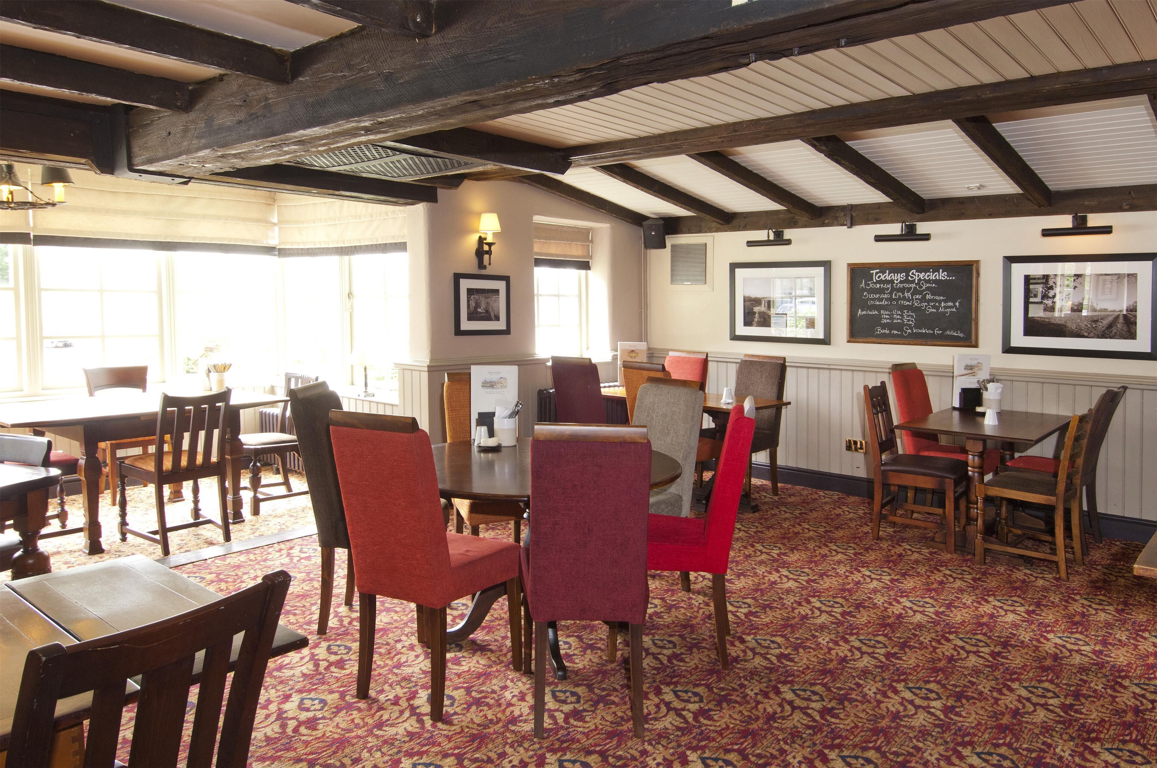 A restaurant with wooden tables and chairs, a patterned carpet, and framed pictures on the walls.