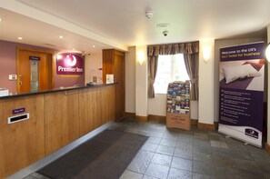 A hotel reception area with a wooden reception desk, a private door, and a sign for Premier Inn. - Premier Inn Manchester - Handforth (Wilmslow)