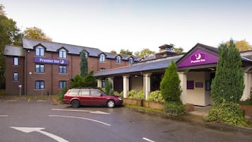 Un hotel Premier Inn con un coche rojo estacionado en la parte delantera, un edificio de ladrillo y una entrada cubierta.