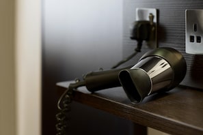A hair dryer on a wooden surface with a power outlet in the background. - Premier Inn Manchester - Wilmslow (Wilmslow)