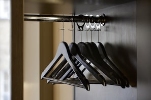 A metal rack with multiple hooks holding black items, likely coats or bags, in a room with a wooden door and a textured wall. - Premier Inn Manchester - Wilmslow (Wilmslow)