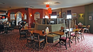 Een restaurant met zitjes, tafels en stoelen, met een kamerbreed tapijt en rode wanden.