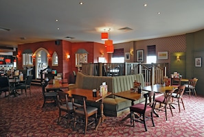 A restaurant with booths, tables, and chairs, featuring a patterned carpet and red walls. - Premier Inn Manchester Tameside Hyde (Hyde)