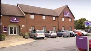 A Premier Inn hotel with a brick facade, double doors, and a parking lot with several cars. - Premier Inn Manchester Trafford Centre Nth (Manchester)