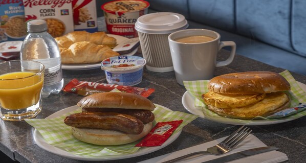 A breakfast table with croissants, sausages, a sandwich, juice, coffee, and cereal boxes.