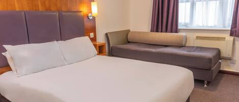 A hotel room with a large bed, a sofa, a nightstand, and a window with curtains.