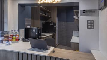 A hotel reception area with a neon sign reading "Check-In," a laptop on the counter, and a sign indicating "Best Western Rewards Members Welcome."
