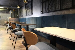 A restaurant interior with booths and tables, wooden chairs, and pendant lighting.