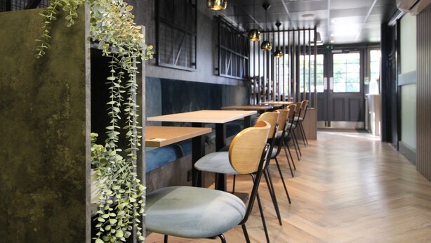 A restaurant interior with wooden tables and chairs, hanging pendant lights, and a view of the outdoors through large windows. - Plaza Hotel, Chorley, Sure Collection by Best Western (Chorley)