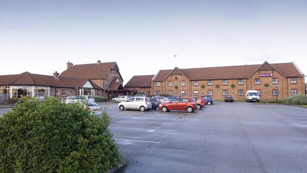 A hotel with multiple buildings, a parking lot with several cars, and a well-maintained hedge. - Premier Inn Manchester - Denton (Manchester)