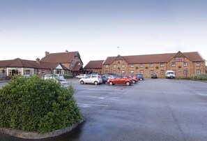 A hotel with multiple buildings, a parking lot with several cars, and a well-maintained hedge. - Premier Inn Manchester - Denton (Manchester)